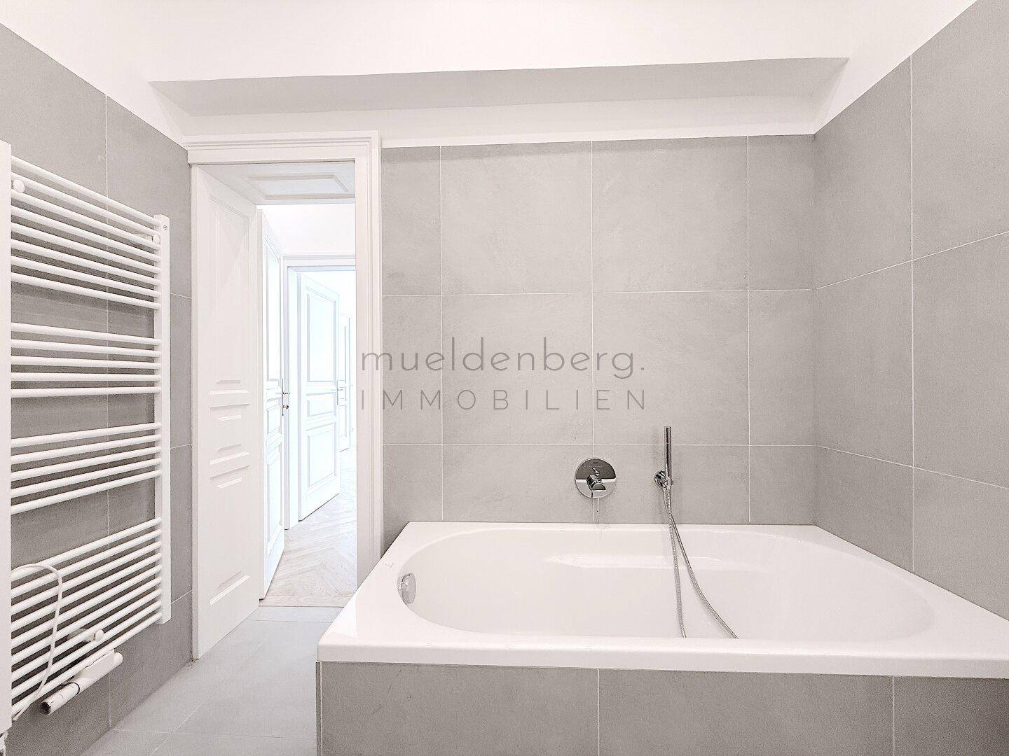 Modernes Badezimmer mit Badewanne und Handtuchheizkörper, in neutralen Grautönen gestaltet.