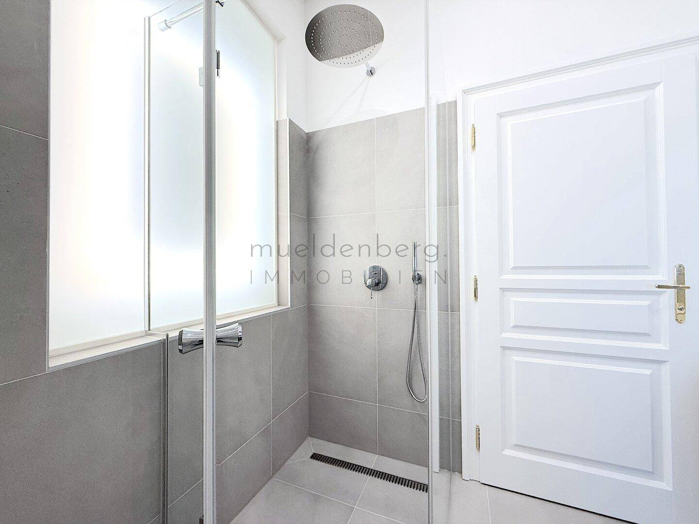 Geräumige, moderne Dusche mit Glasabtrennung und Regenduschkopf in einem hell gefliesten Bad.