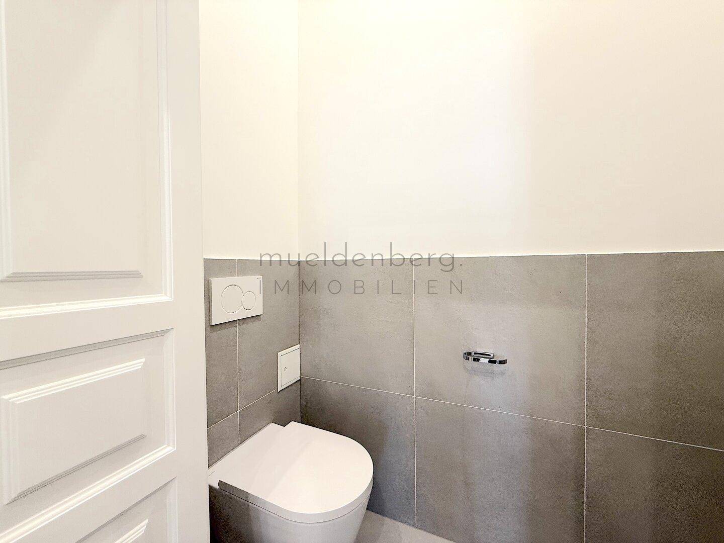 Separate Gästetoilette mit Wand-WC und modernen grauen Fliesen, minimalistisch gestaltet.