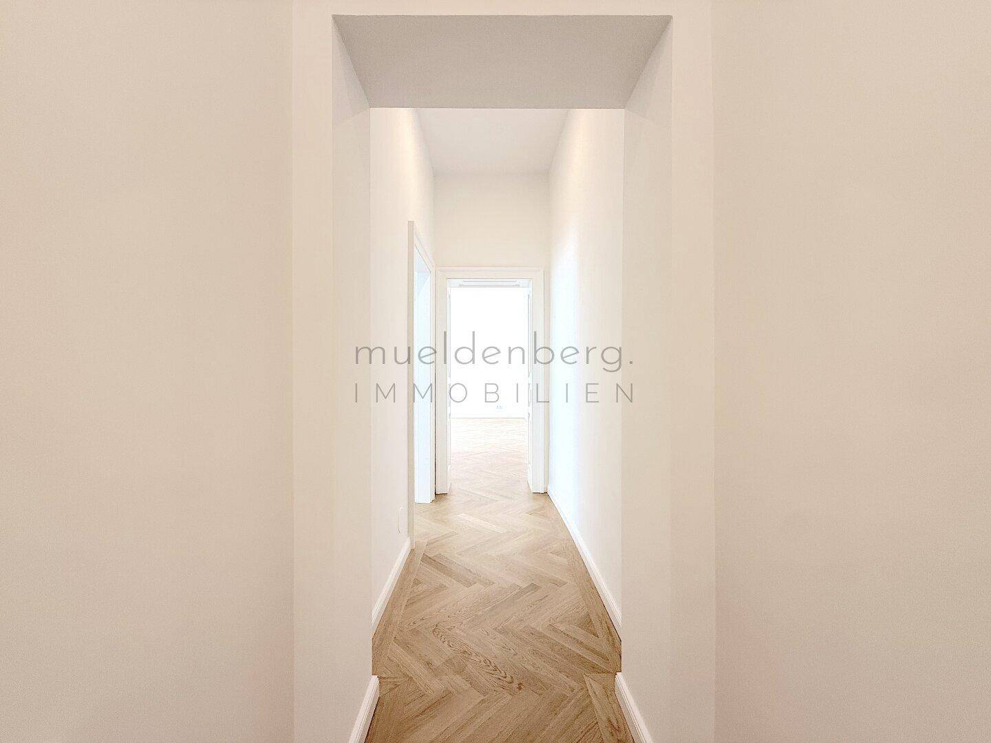 Langer, heller Flur mit Fischgrätparkett, der zu weiteren Räumen der Wohnung führt.