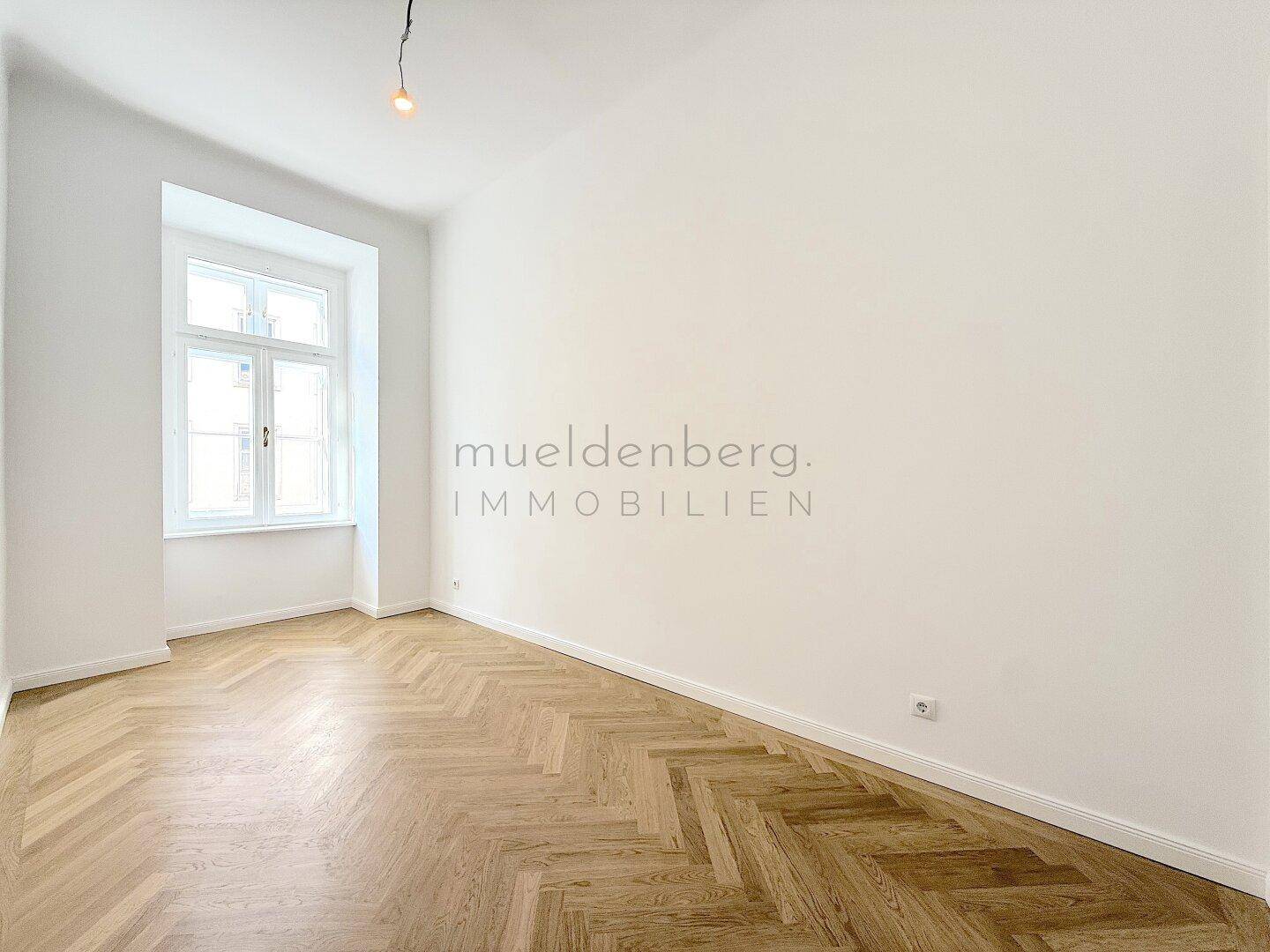 Helles, leeres Zimmer mit Fischgrätparkett und einem hohen Fenster, bereit zur Einrichtung.