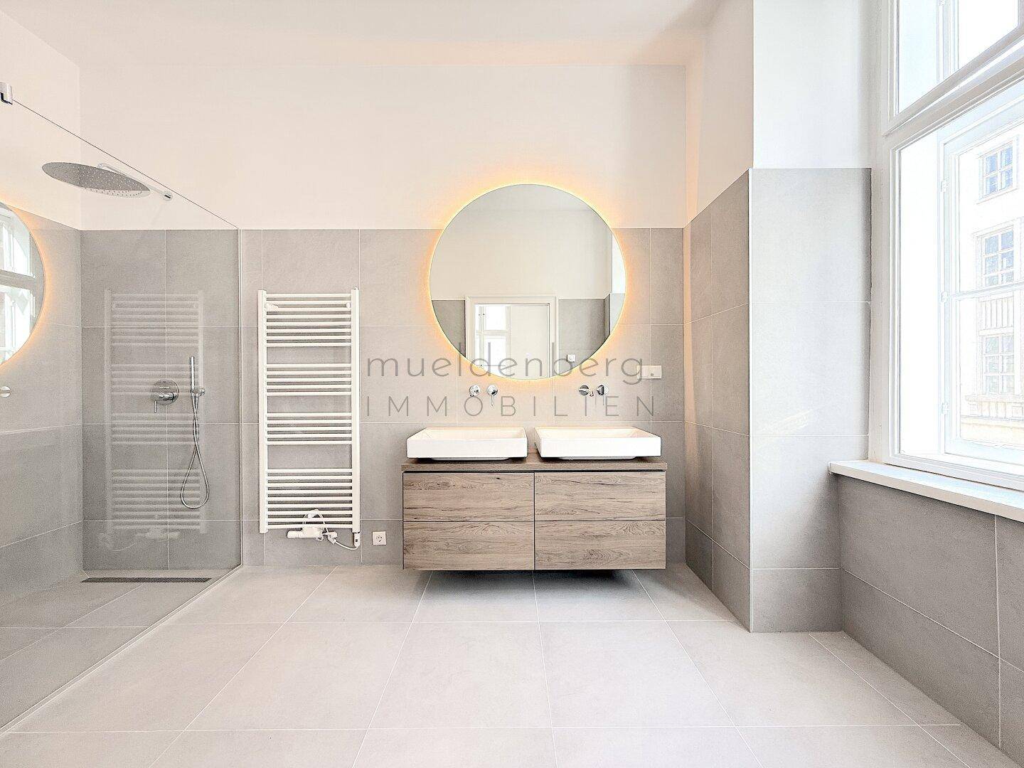 Modernes Badezimmer mit Doppelwaschbecken, großer begehbarer Dusche und beleuchtetem Spiegel.