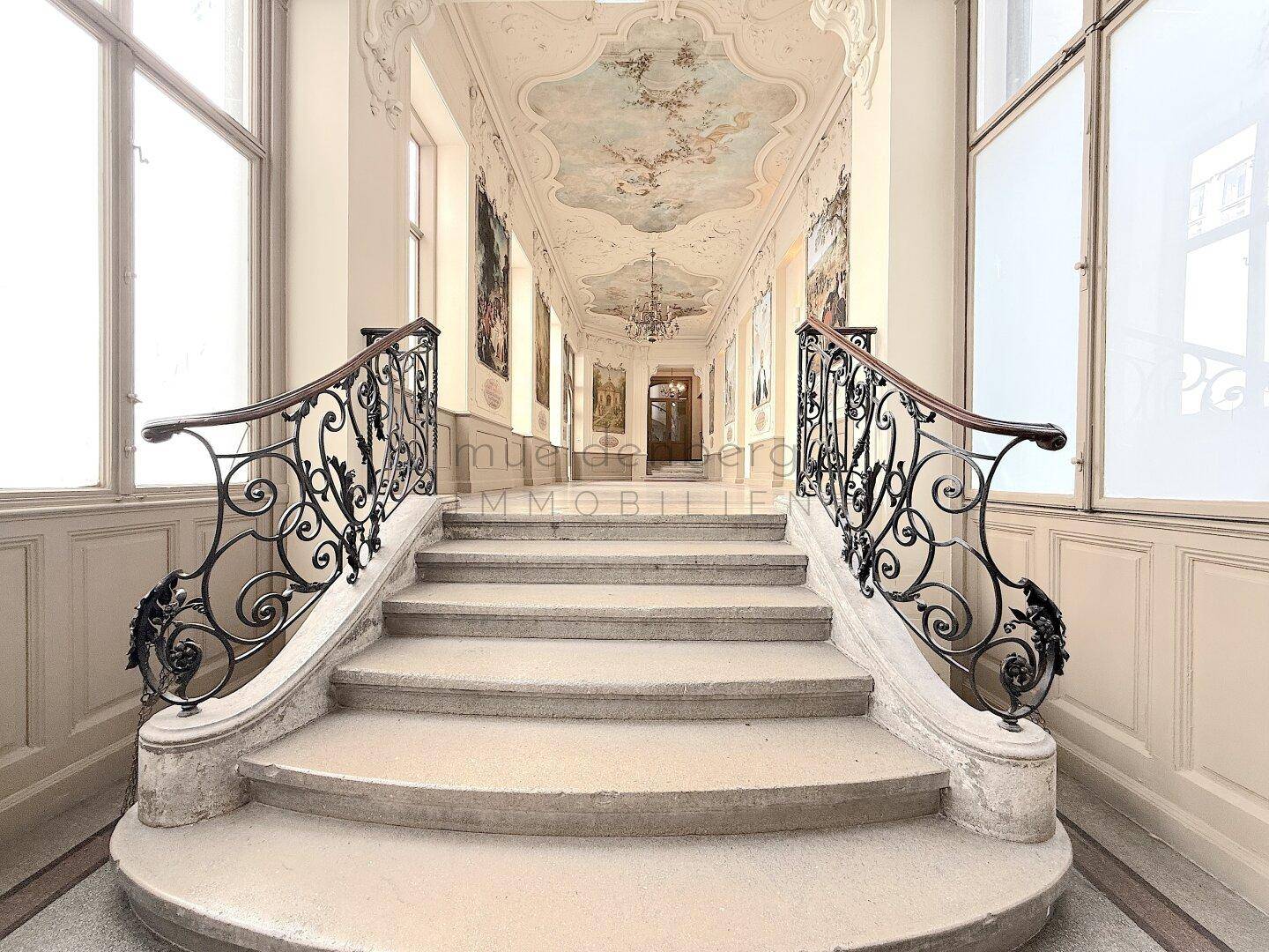 Beeindruckendes Treppenhaus mit aufwendiger Deckenmalerei und schmiedeeisernen Geländern, zeugt von Eleganz.