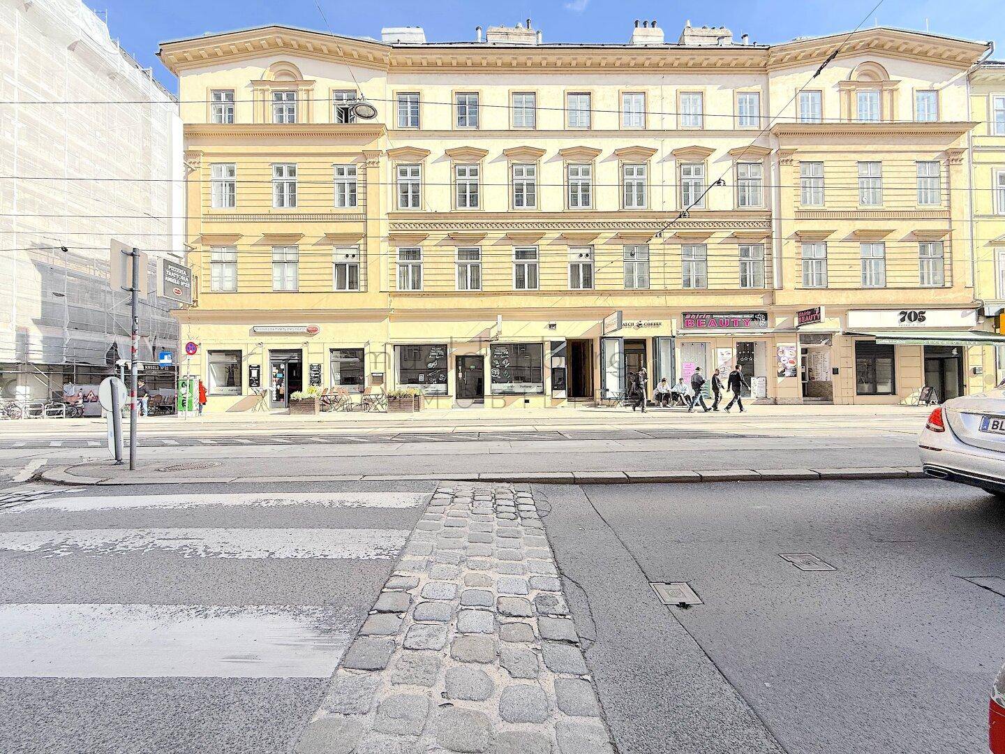 Mehrstöckiges Gebäude mit gelber Fassade an einer belebten Straße, umgeben von städtischer Architektur.