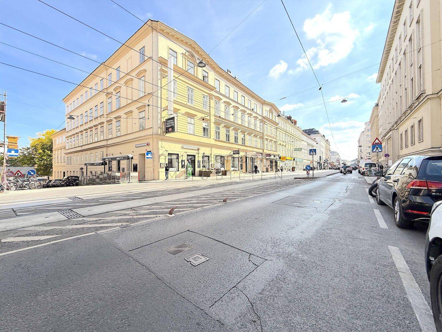 Weitläufige Straßenansicht des Eckgebäudes mit gelber Fassade in einer städtischen Umgebung.