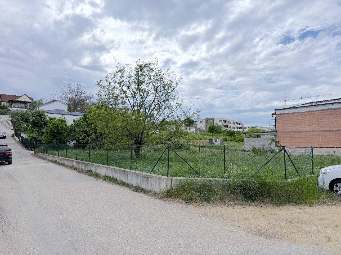 Unbebautes Grundstück an einer Straße mit Blick auf weitere Gebäude in der Umgebung.