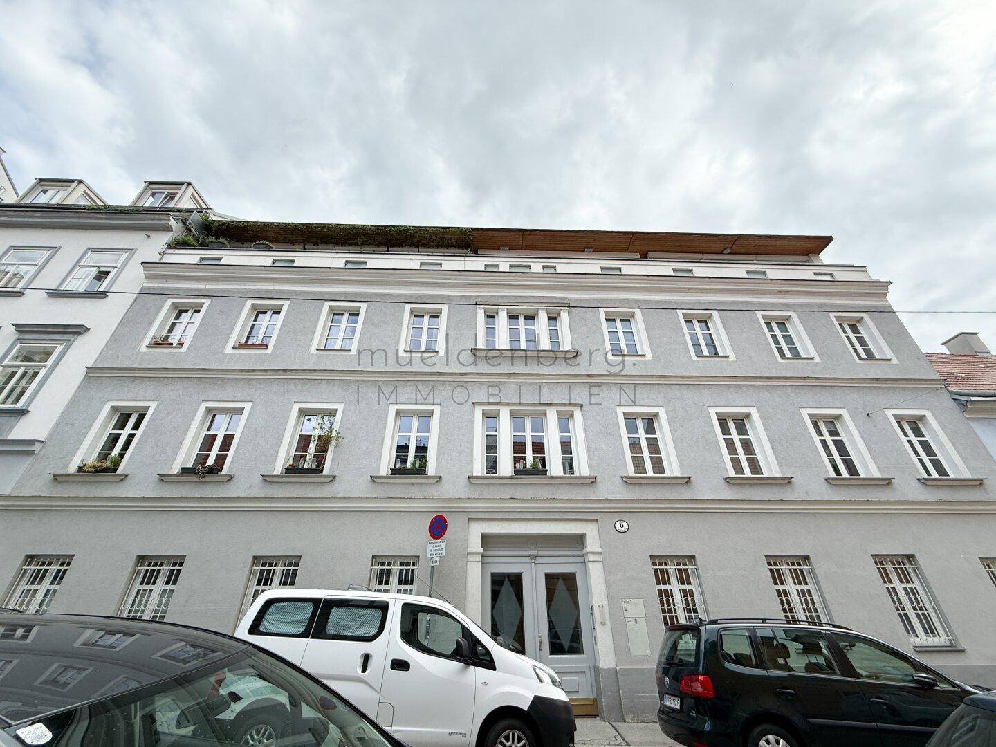 Historische Fassade eines Mehrfamilienhauses mit vielen Fenstern und geparkten Autos.