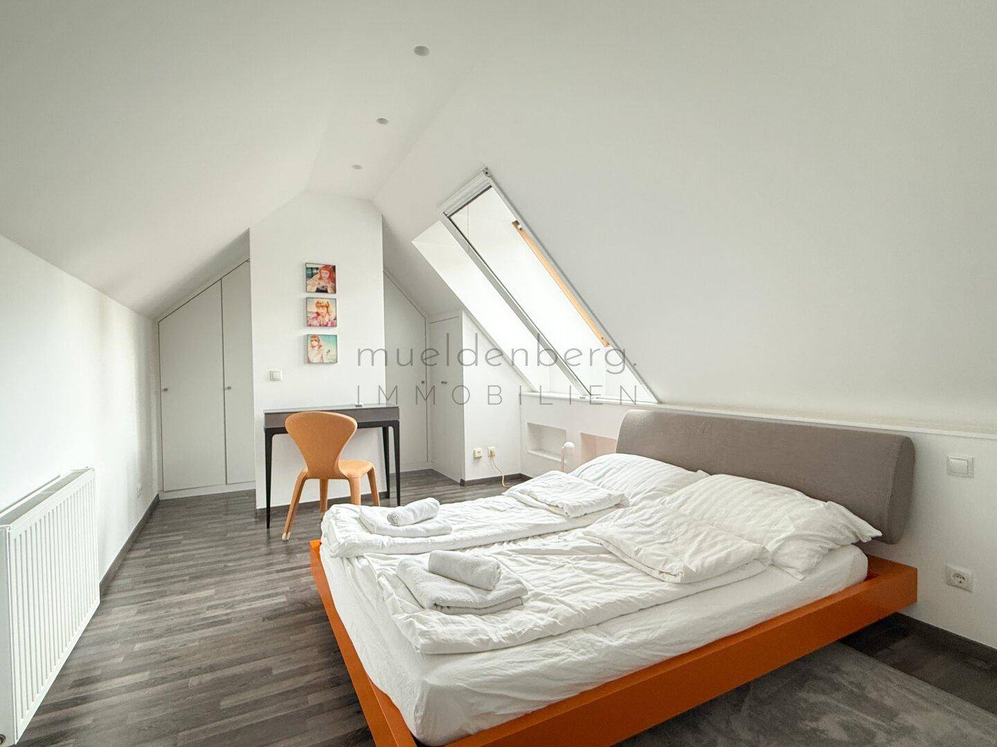 Helles Schlafzimmer im Dachgeschoss mit Dachfenster und Holzboden.