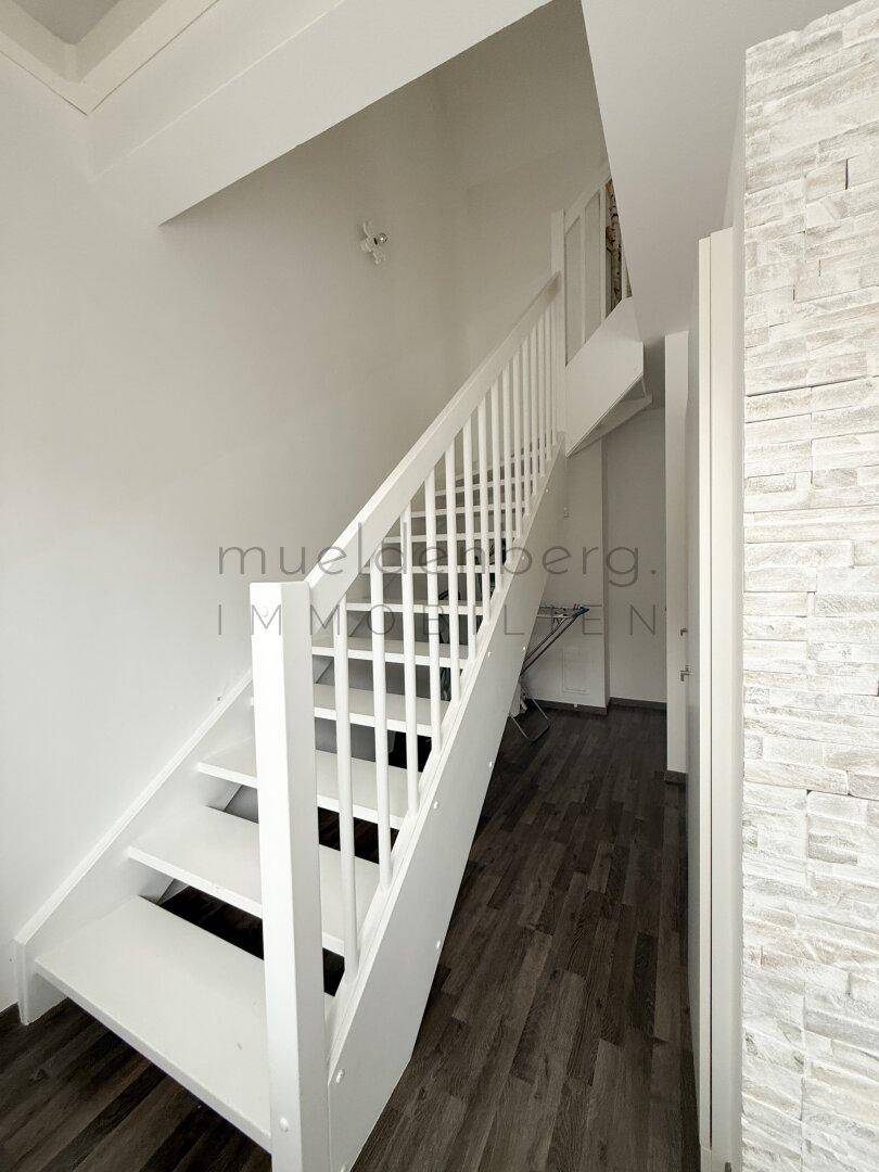 Weiß gestrichene Holztreppe mit modernem Geländer und Steinwandakzent.