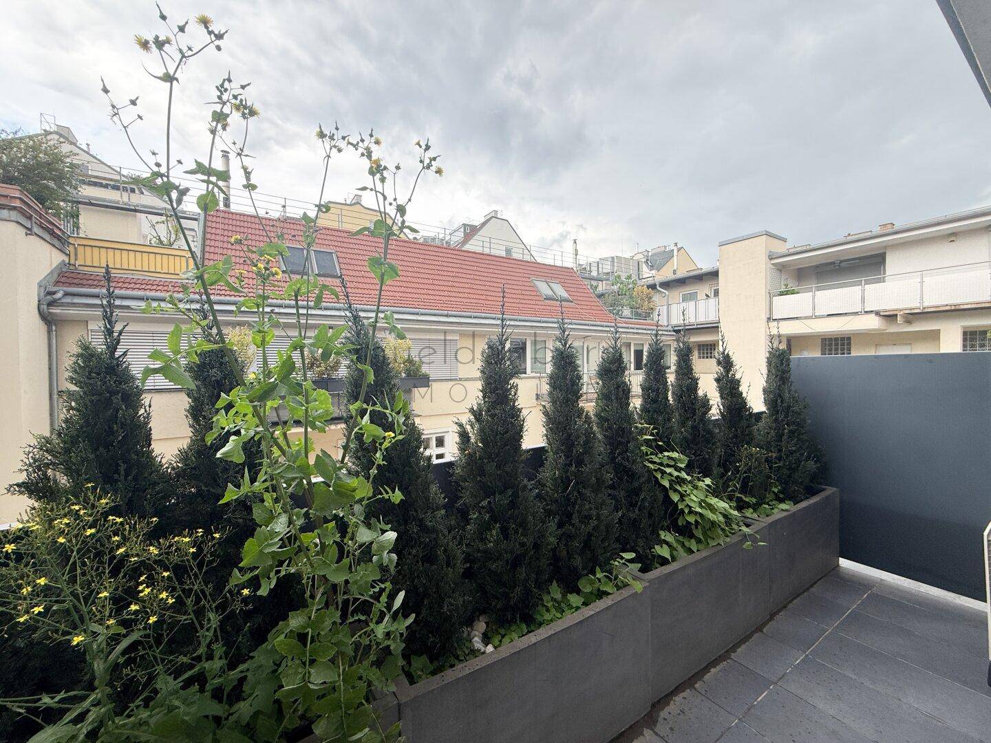 Kleiner Balkon mit grünen Pflanzen und Blick auf umliegende Gebäude.