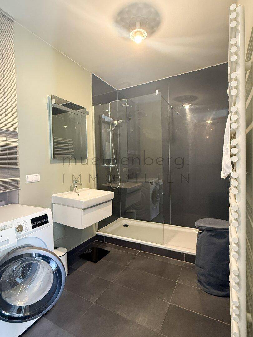 Modernes Badezimmer mit Dusche, Waschmaschine und beheiztem Handtuchhalter.
