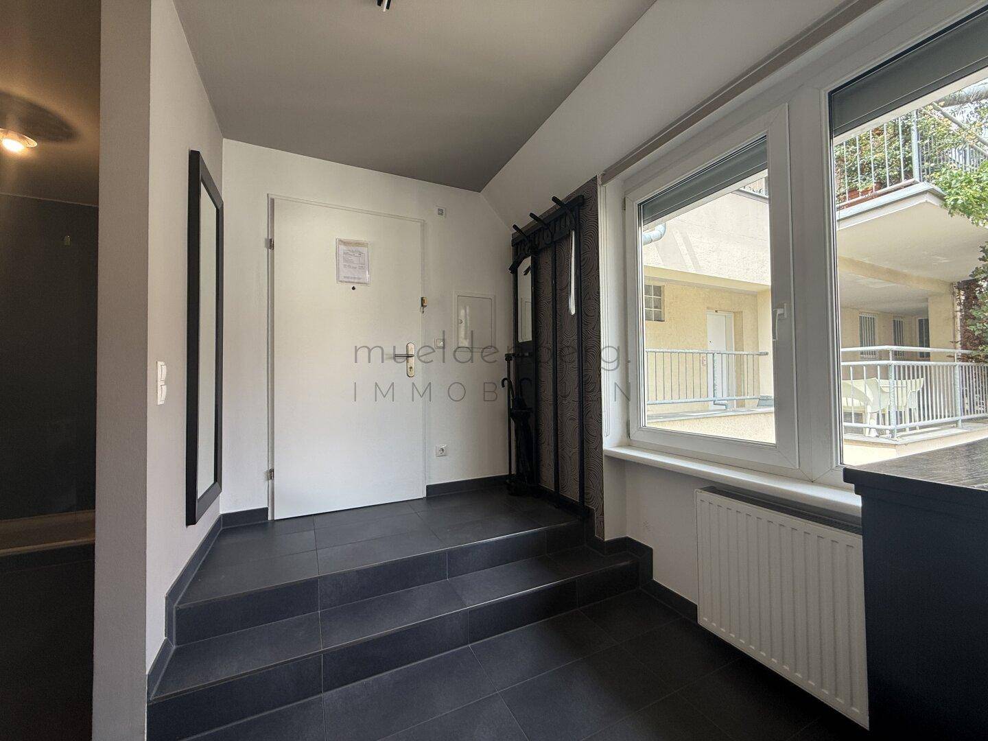 Eingangsbereich mit dunklen Fliesen, Garderobe und Blick auf den Innenhof.