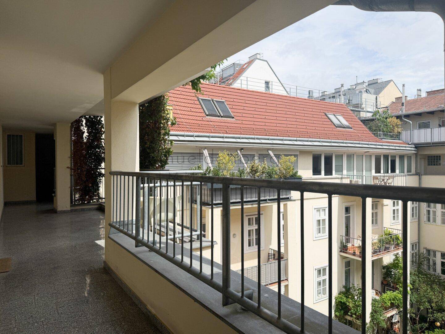 Überdachte Loggia mit Geländer und Blick auf den begrünten Innenhof.