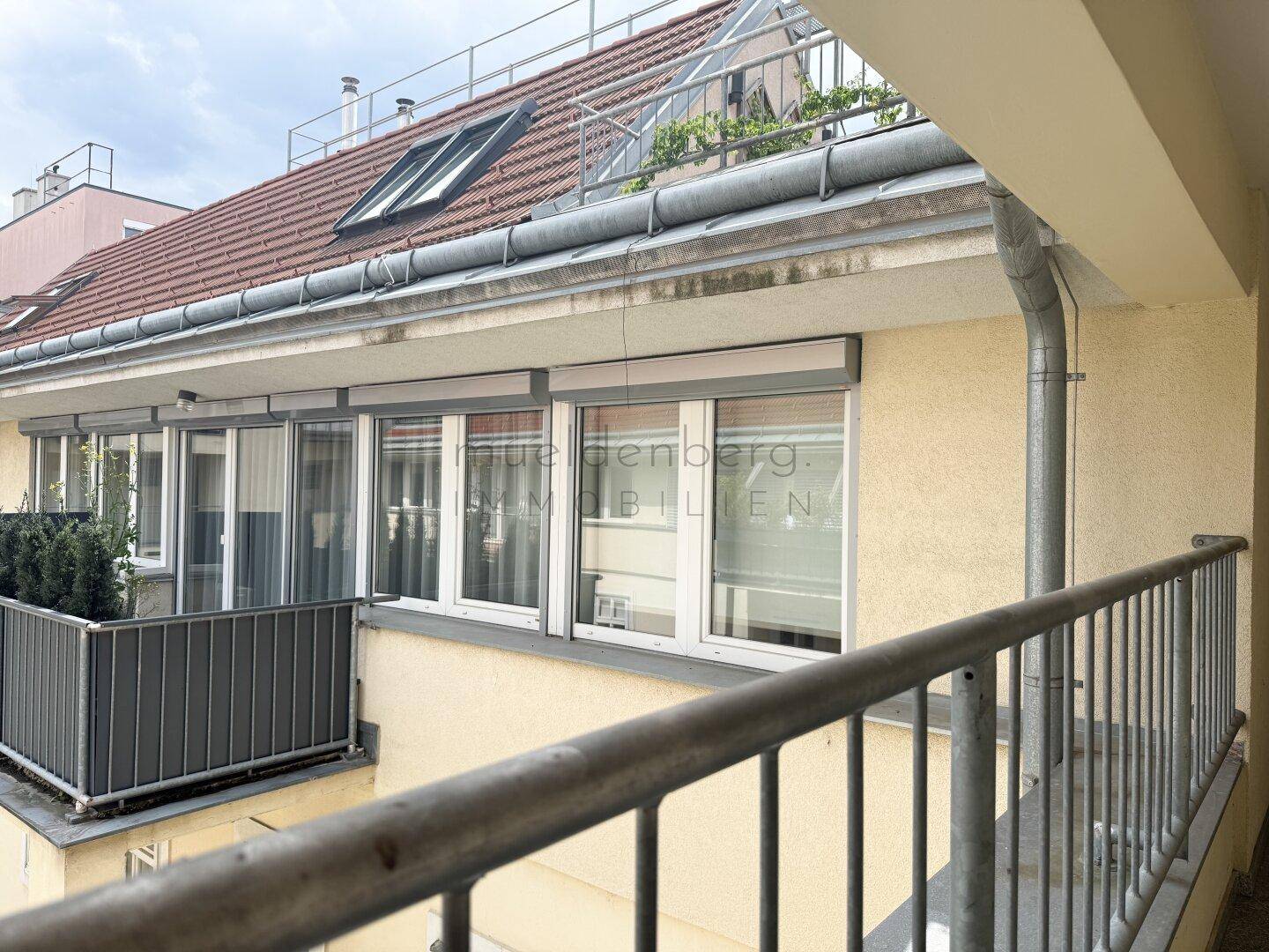 Balkon mit Metallgeländer und Blick auf die umliegenden Dächer und Gebäude.