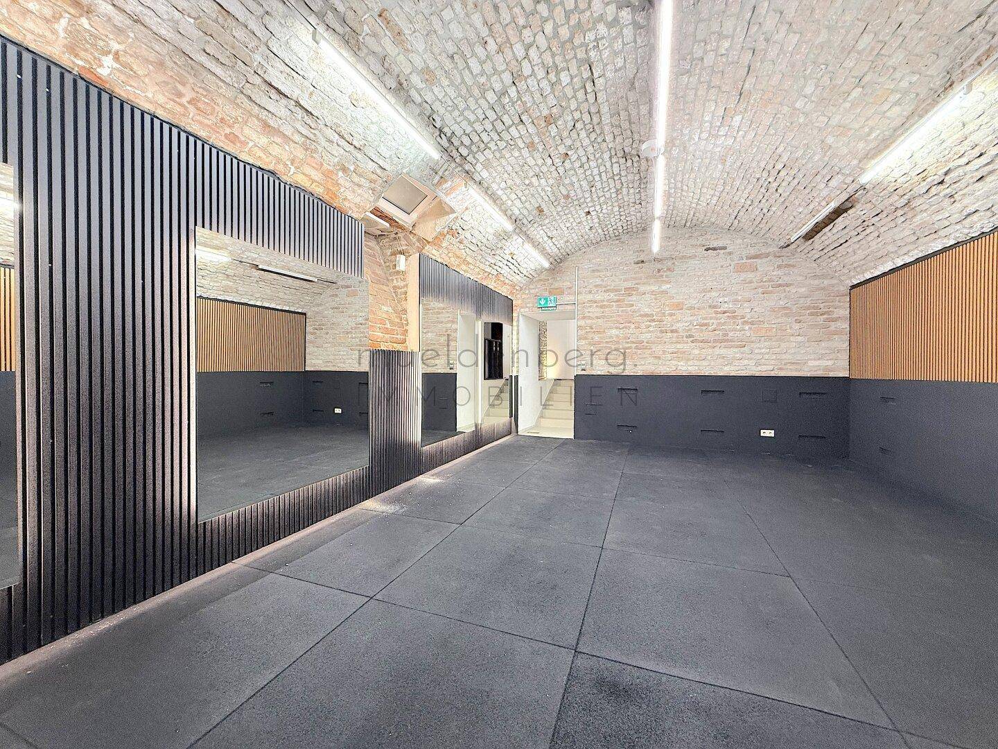 Weitläufiger Raum mit Ziegelgewölbedecke, dunklem Boden und modernen Spiegelelementen.