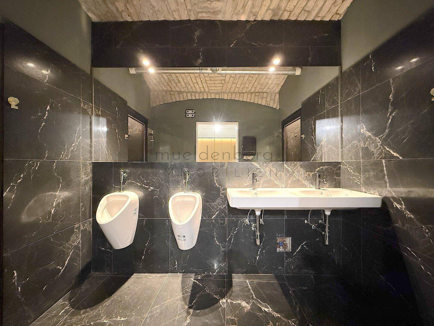 Modernes Badezimmer mit dunklen Marmorfliesen, zwei Urinalen und Doppelwaschbecken.