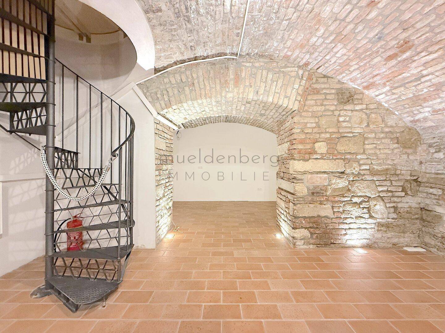 Geräumiger Raum mit Ziegelgewölbedecke und Terrakottafliesen, akzentuiert durch eine Wendeltreppe.