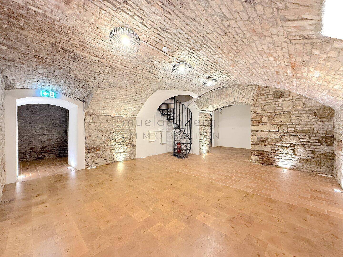Historischer Raum mit Ziegelgewölbe, freigelegten Steinwänden und einer eleganten Wendeltreppe.