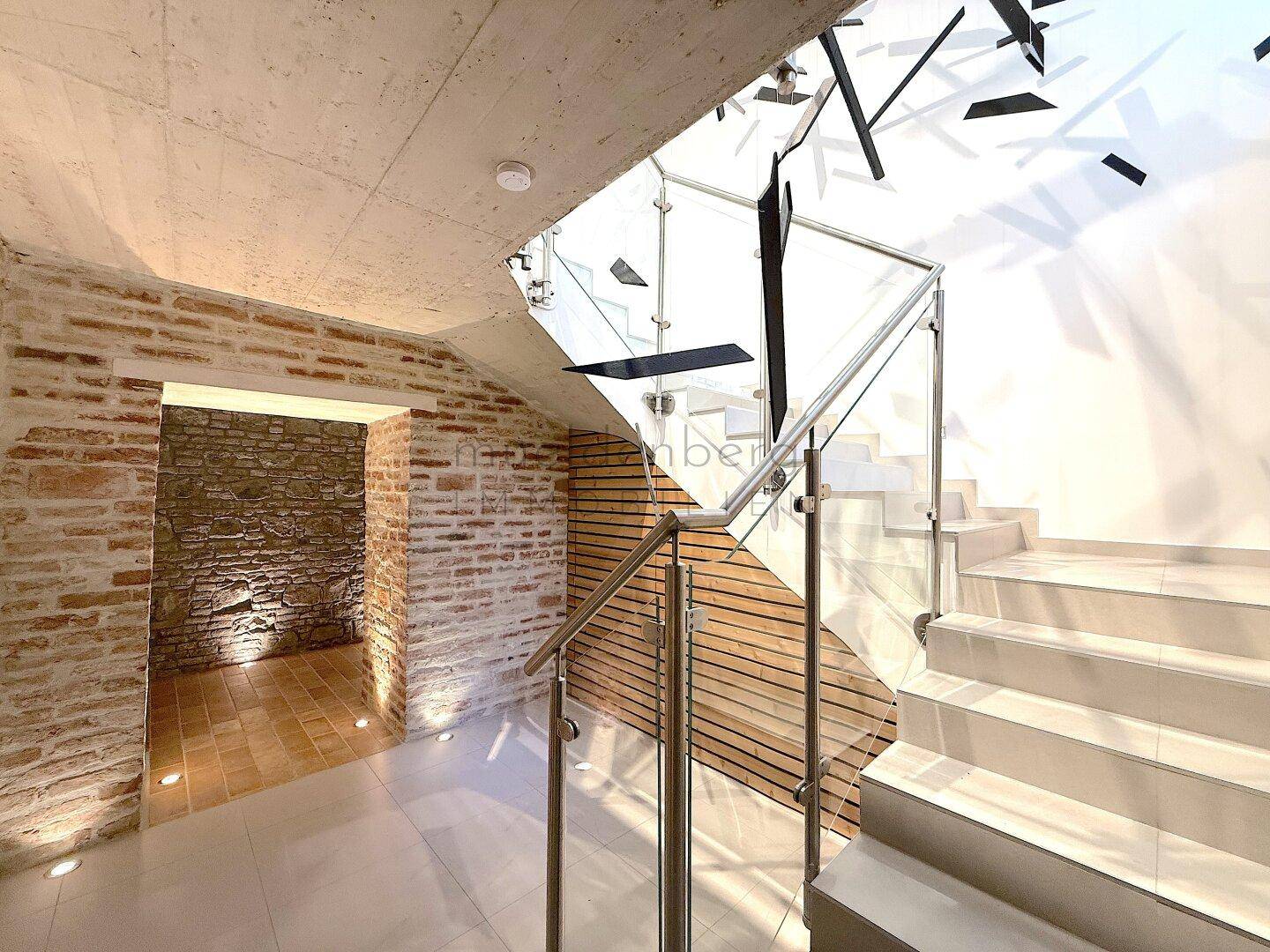 Moderne Treppe mit Glasgeländer und freigelegten Ziegelwänden in einem hellen Eingangsbereich.