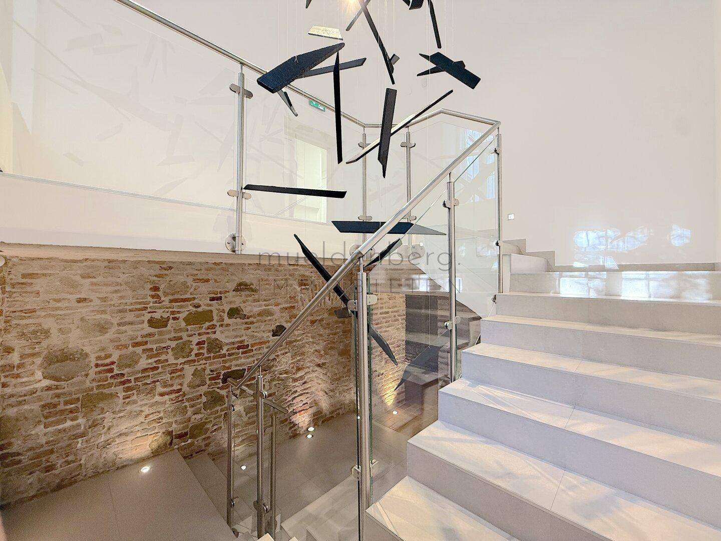 Elegante Treppe mit Glasgeländer und freigelegter Ziegelwand, die einen modernen Kontrast bildet.