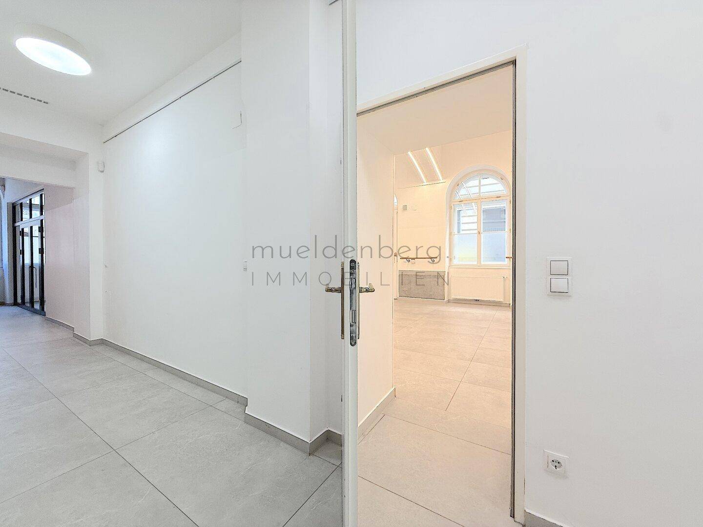 Heller Flur mit einer Glastür, die den Blick in einen weiteren Raum mit großen Fenstern freigibt.