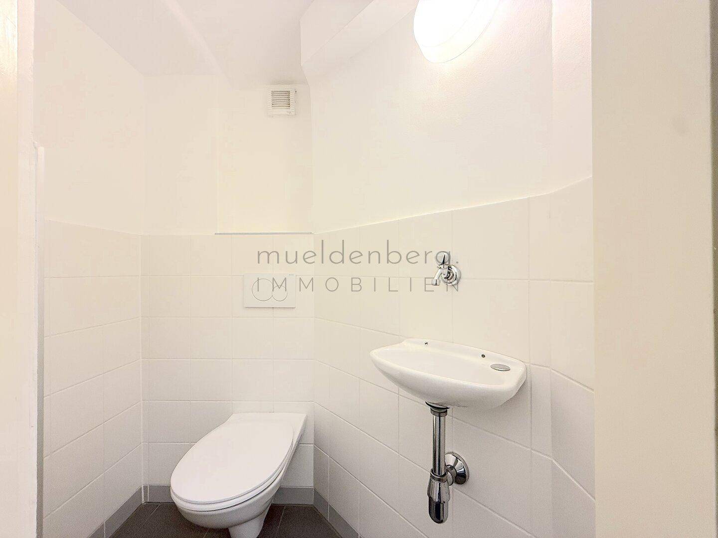 Kleines, hell gefliestes Gäste-WC mit wandhängender Toilette und modernem Handwaschbecken.