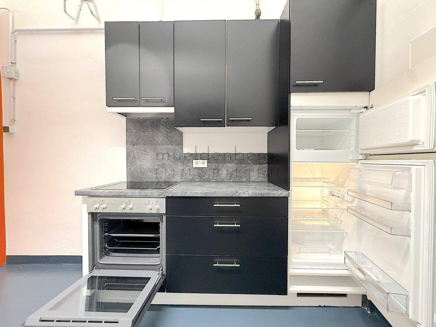 Voll ausgestattete Küchenzeile mit schwarzen Schränken, Backofen und offenem Kühlschrank.