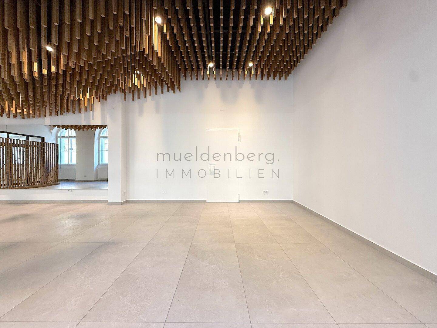 Geräumiger Gewerberaum mit Holzlamellendecke, weiß gestrichenen Wänden und Fliesenboden.