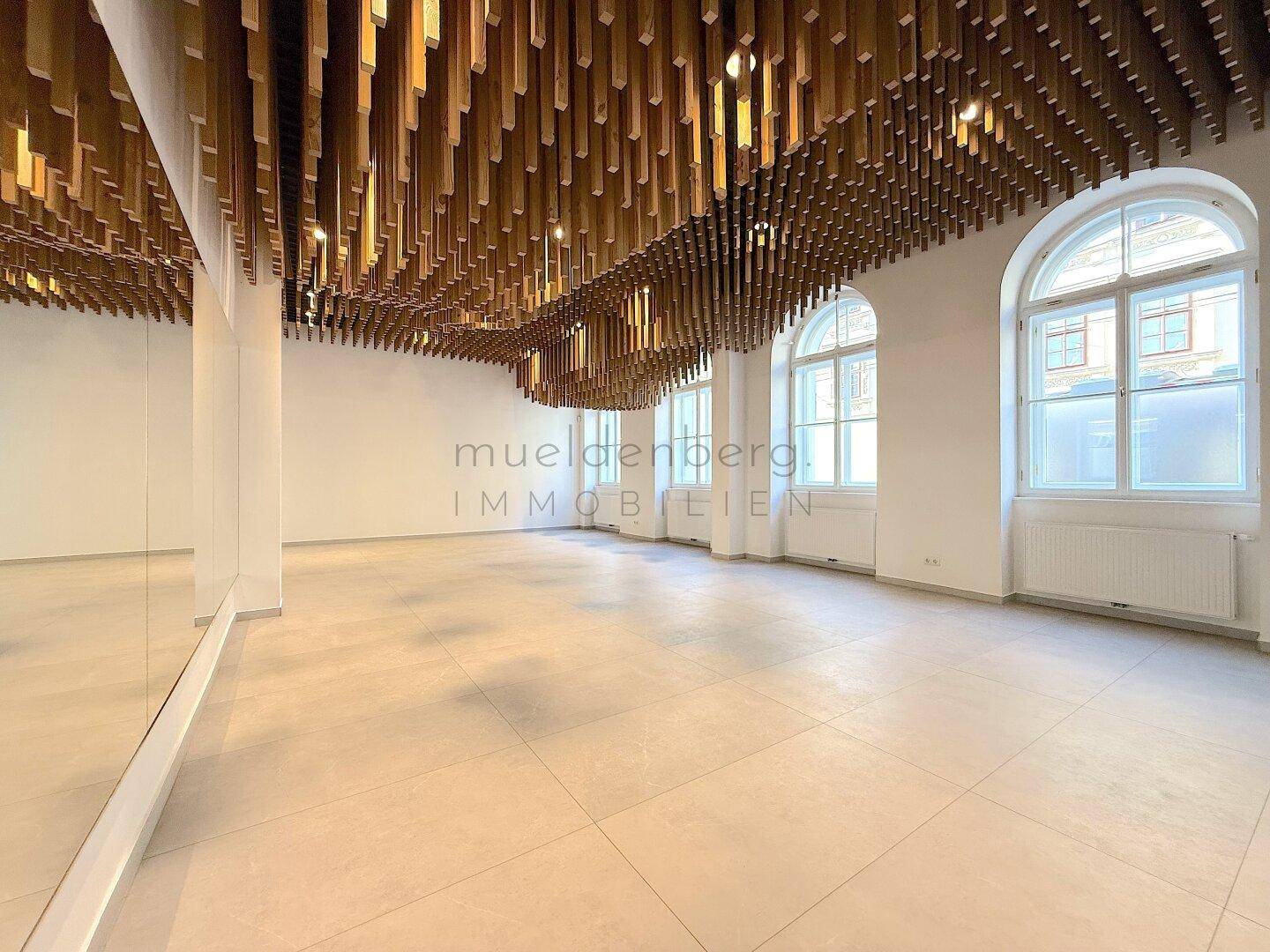 Geräumiger Gewerberaum mit großen Fenstern, Spiegelwand und auffälliger Holzlamellendecke.