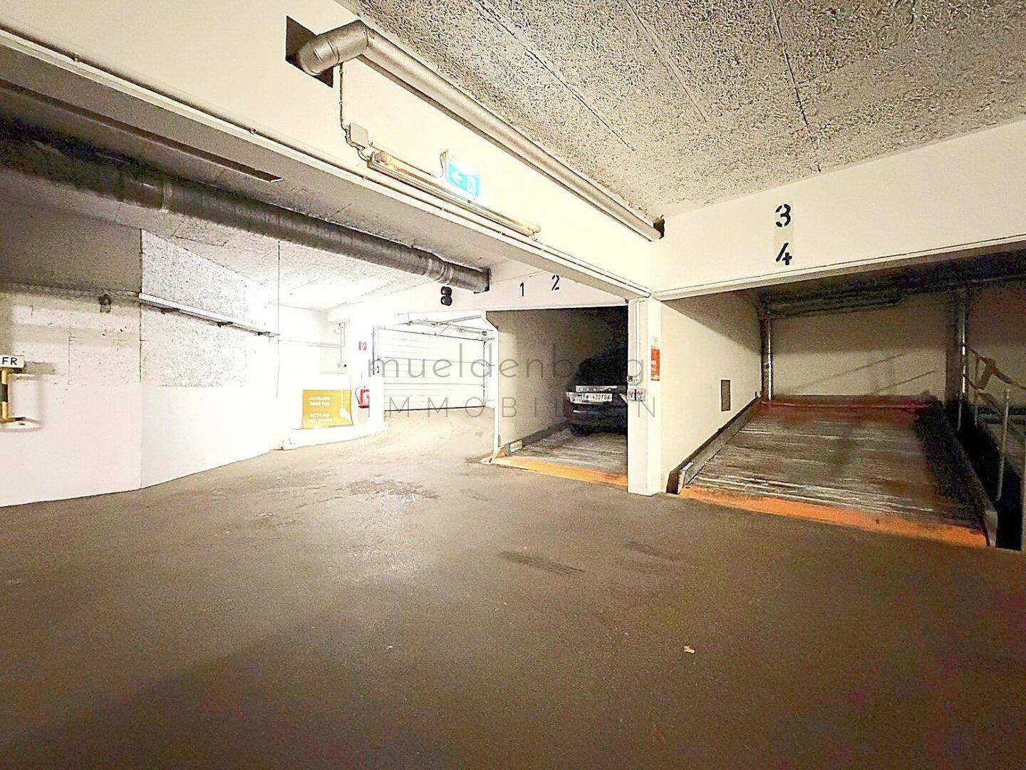 Eingangsbereich einer Tiefgarage mit mechanischem Parksystem und weiteren Stellplätzen im Hintergrund.