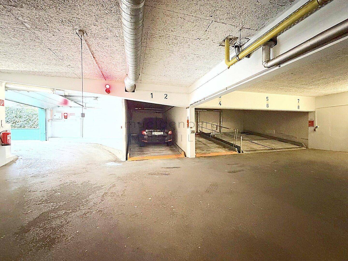 Geräumige Tiefgarage mit mehreren mechanischen Parksystemen und der Zufahrtsrampe.
