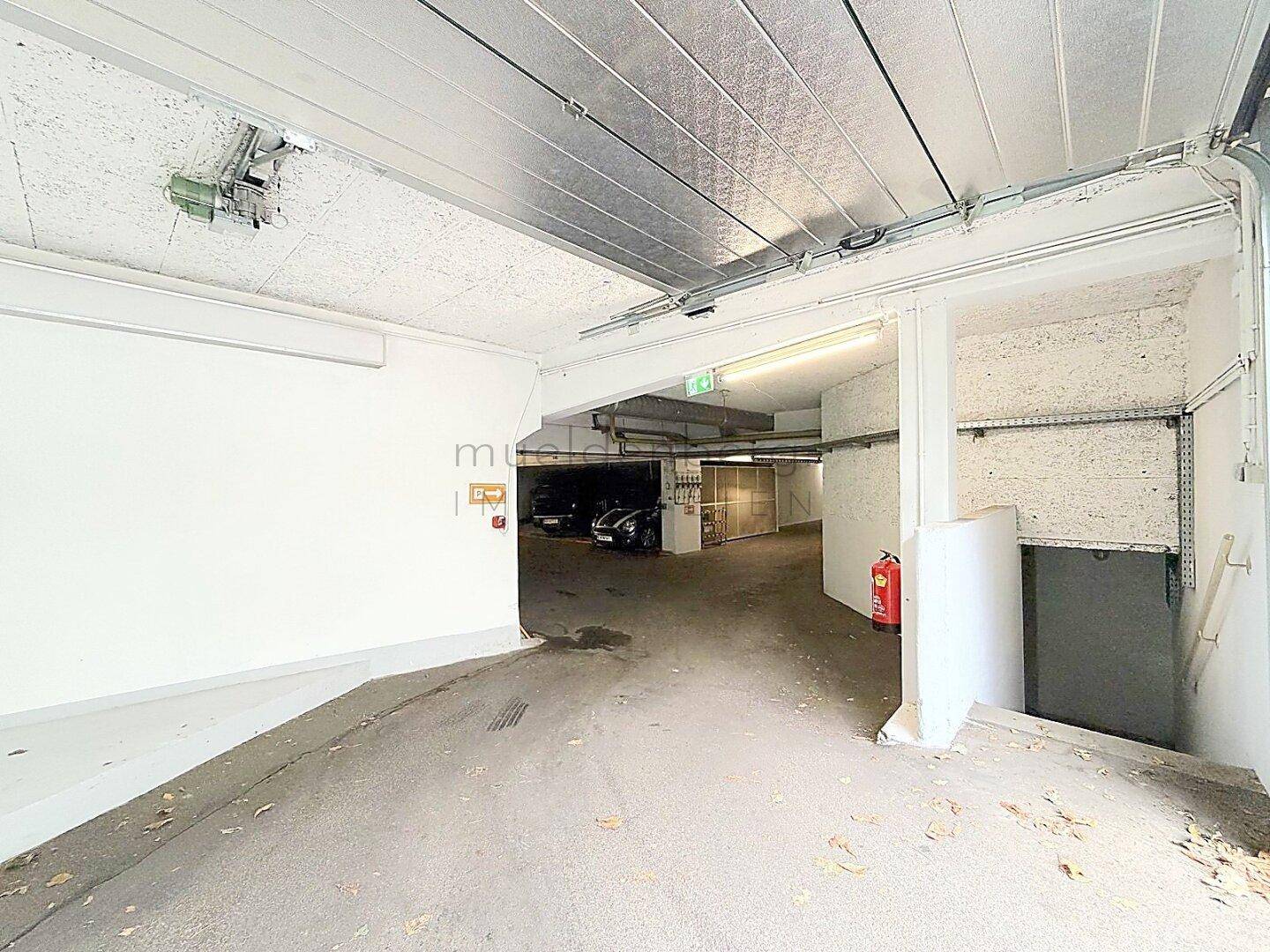 Innenansicht einer Tiefgarage mit Zufahrtsrampe und Sicherheitsausrüstung wie einem Feuerlöscher.