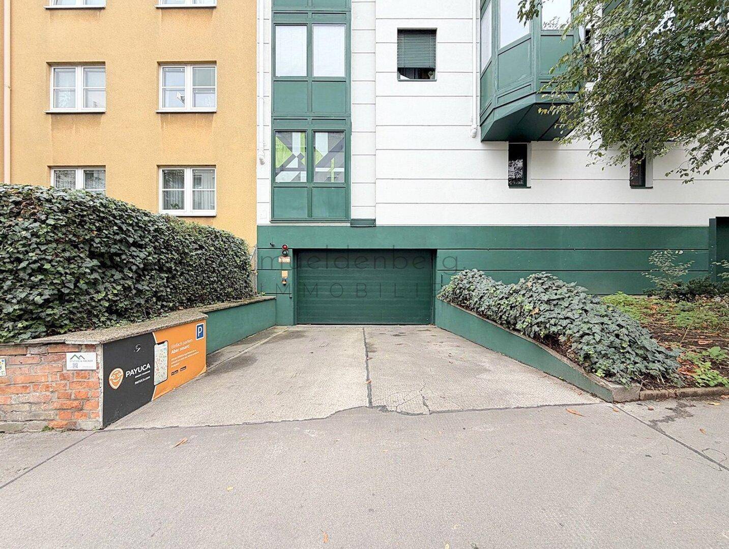 Geschlossenes Garagentor einer Tiefgarage mit grüner Fassade und gepflegten Sträuchern.