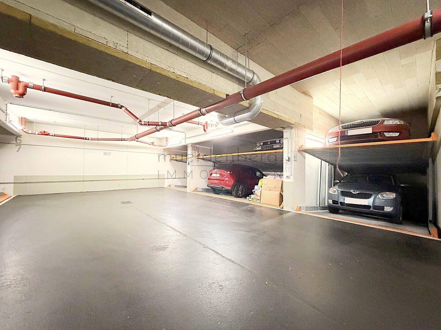 Tiefgarage mit hydraulischen Parksystemen und sichtbaren Versorgungsleitungen an der Decke.