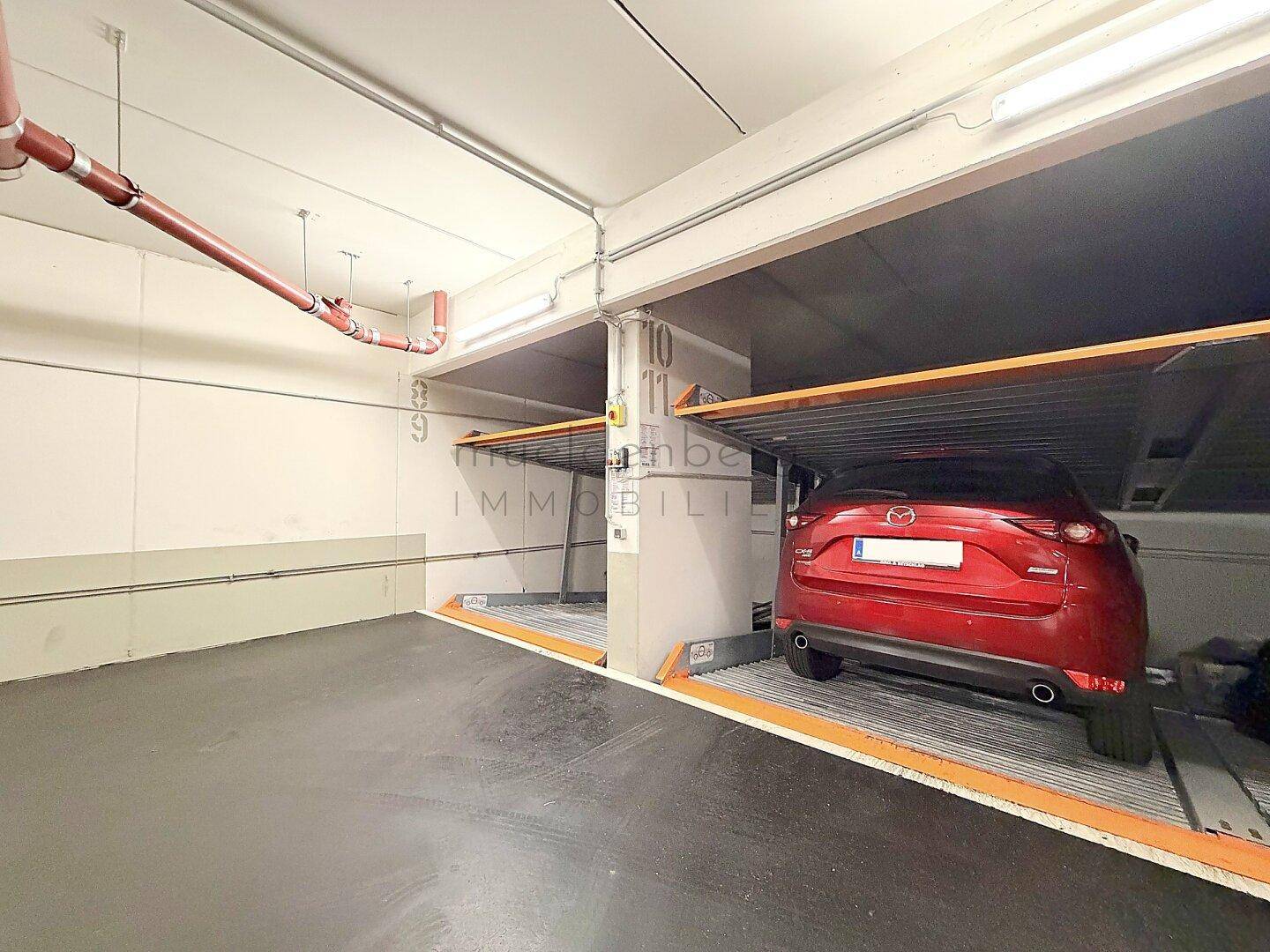Hydraulisches Parksystem in einer Tiefgarage mit einem roten Auto auf der unteren Ebene.