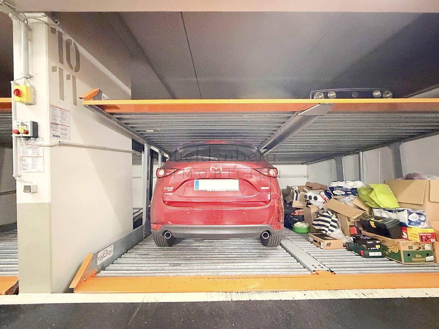 Rotes Auto auf der oberen Ebene eines hydraulischen Parksystems in einer Tiefgarage.