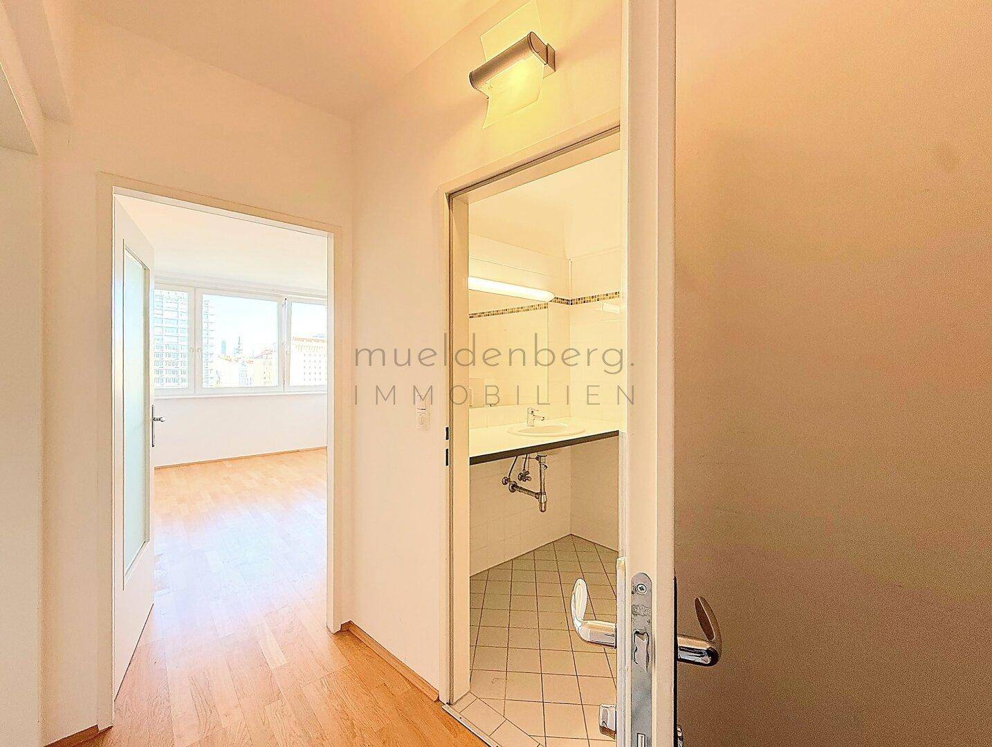 Blick vom Flur in ein Badezimmer und einen hellen Wohnbereich.