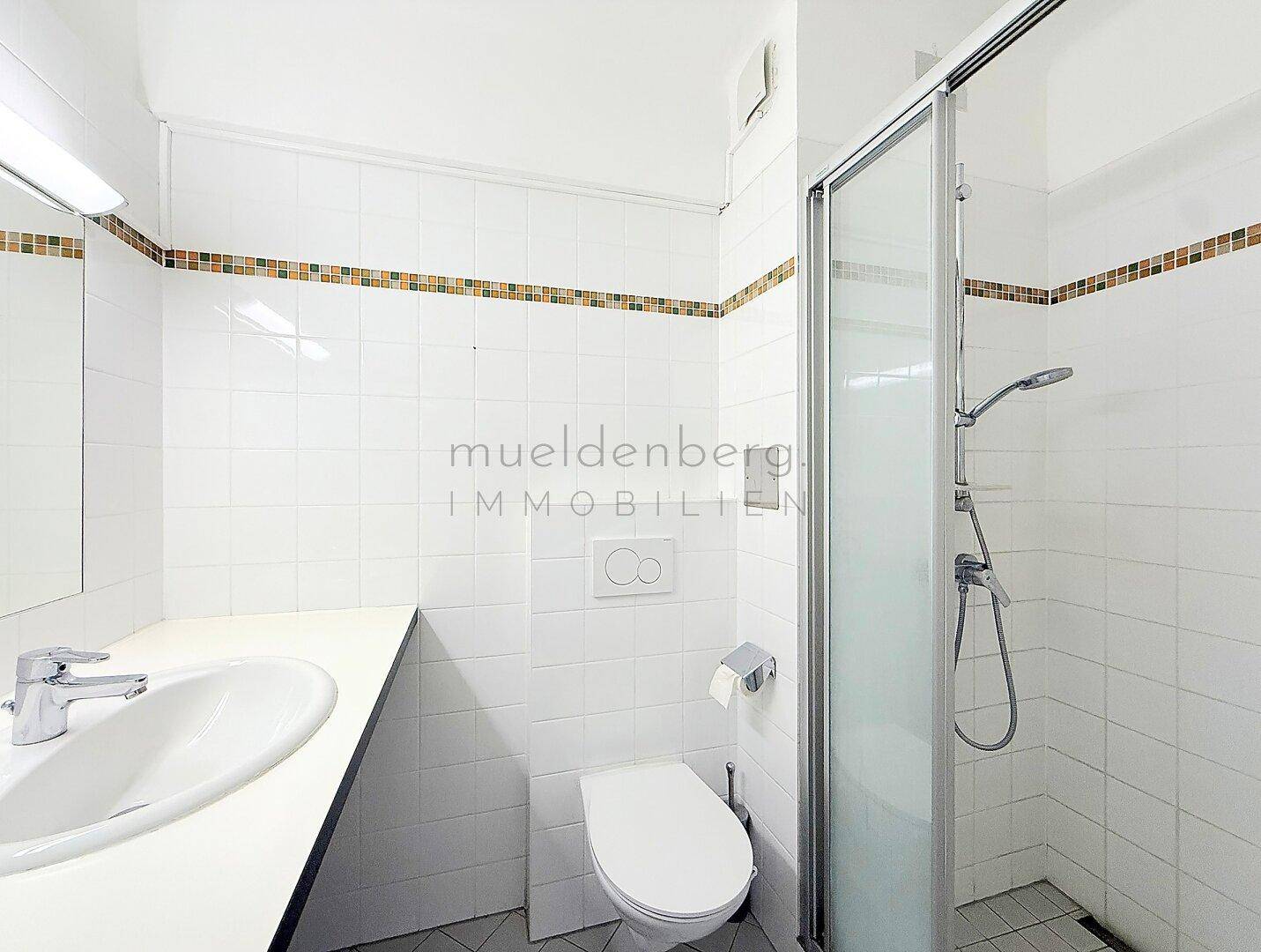 Helles Badezimmer mit Duschkabine, Waschbecken und WC, komplett gefliest.