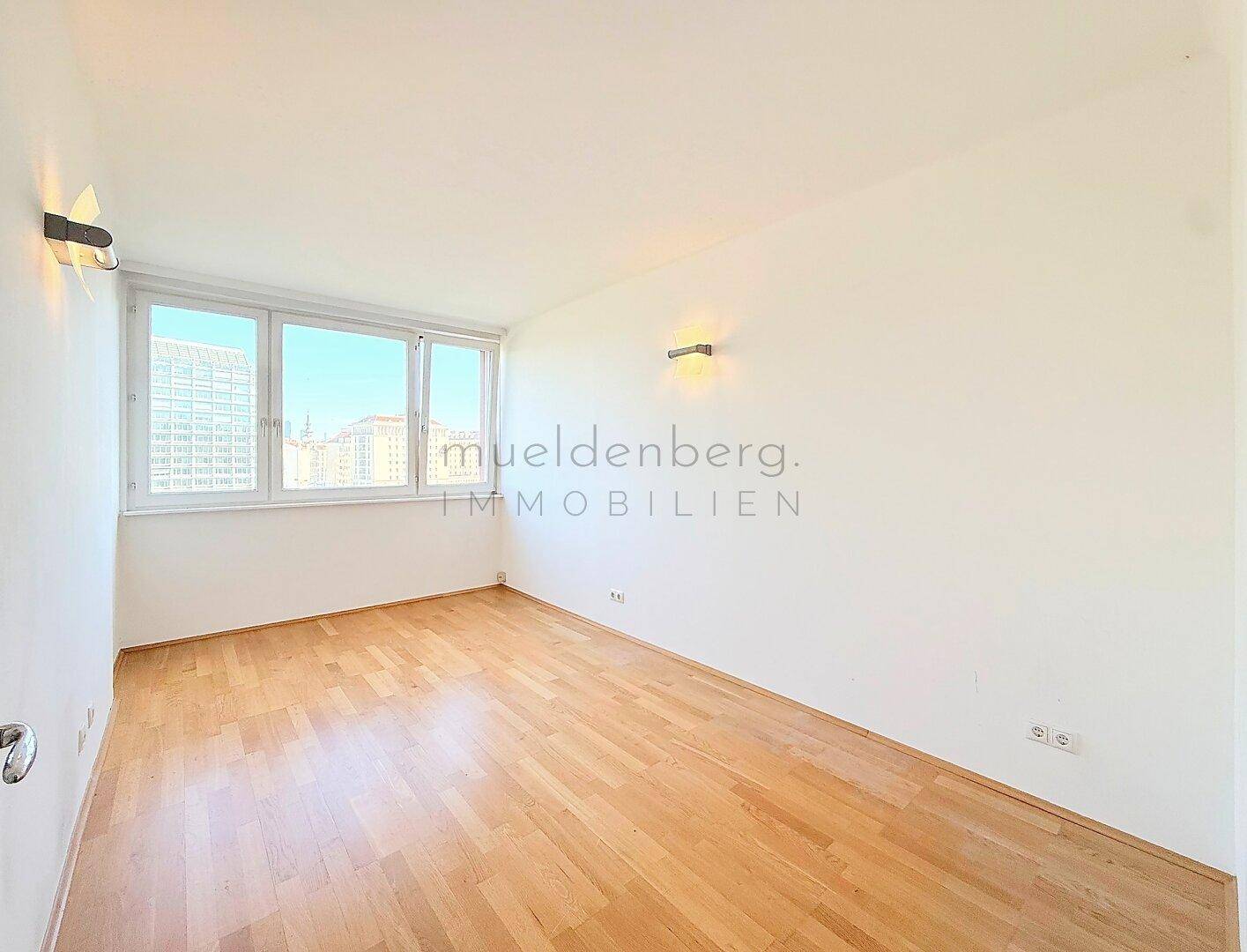 Leeres Zimmer mit hellem Parkettboden und großen Fenstern für viel Tageslicht.