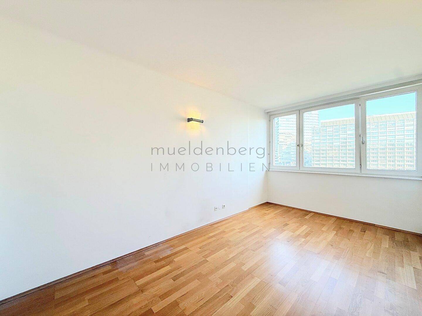 Geräumiges Zimmer mit Parkettboden und breiter Fensterfront, die den Raum erhellt.