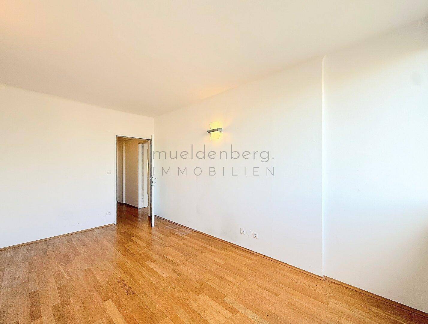 Heller Wohnraum mit Parkettboden und Zugang zu einem weiteren Zimmer.