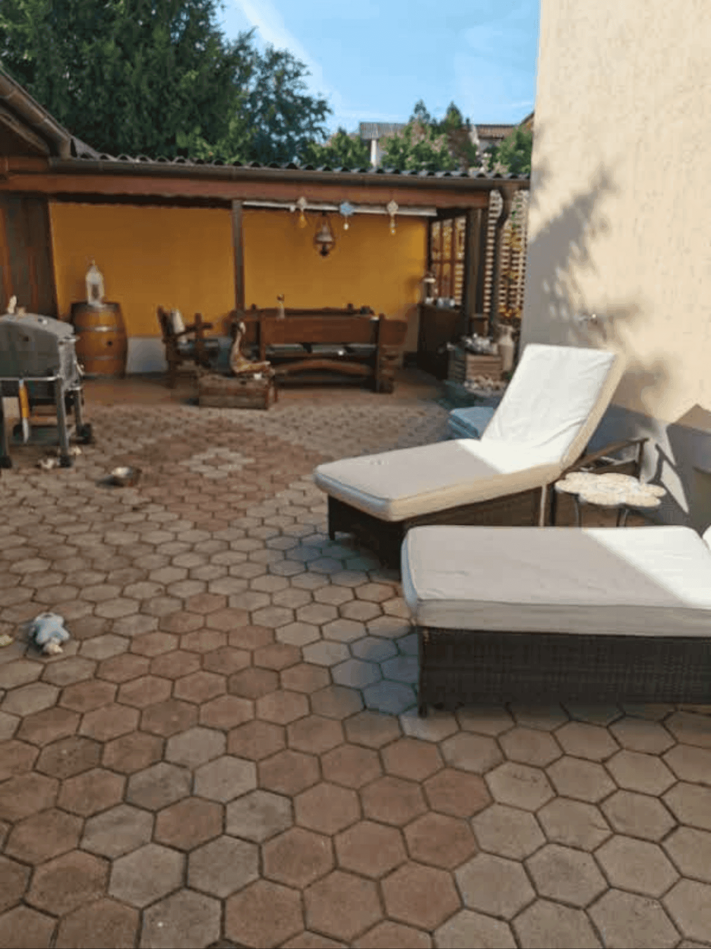 Geräumige Terrasse mit Sonnenliegen und einem überdachten Sitzbereich mit gelber Wand.