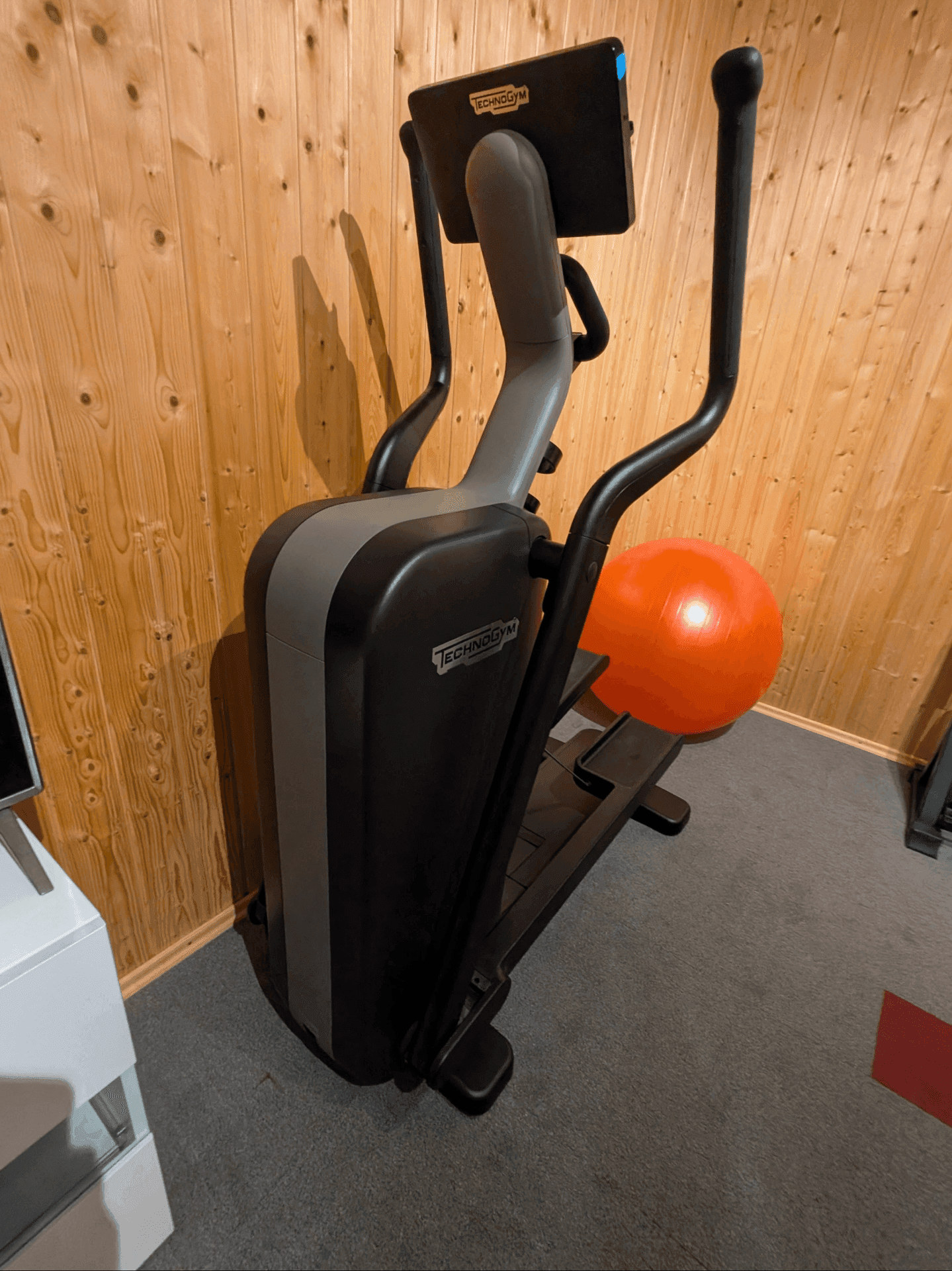 Kleiner Fitnessbereich mit einem Crosstrainer und einem Gymnastikball, umgeben von Holzvertäfelung.