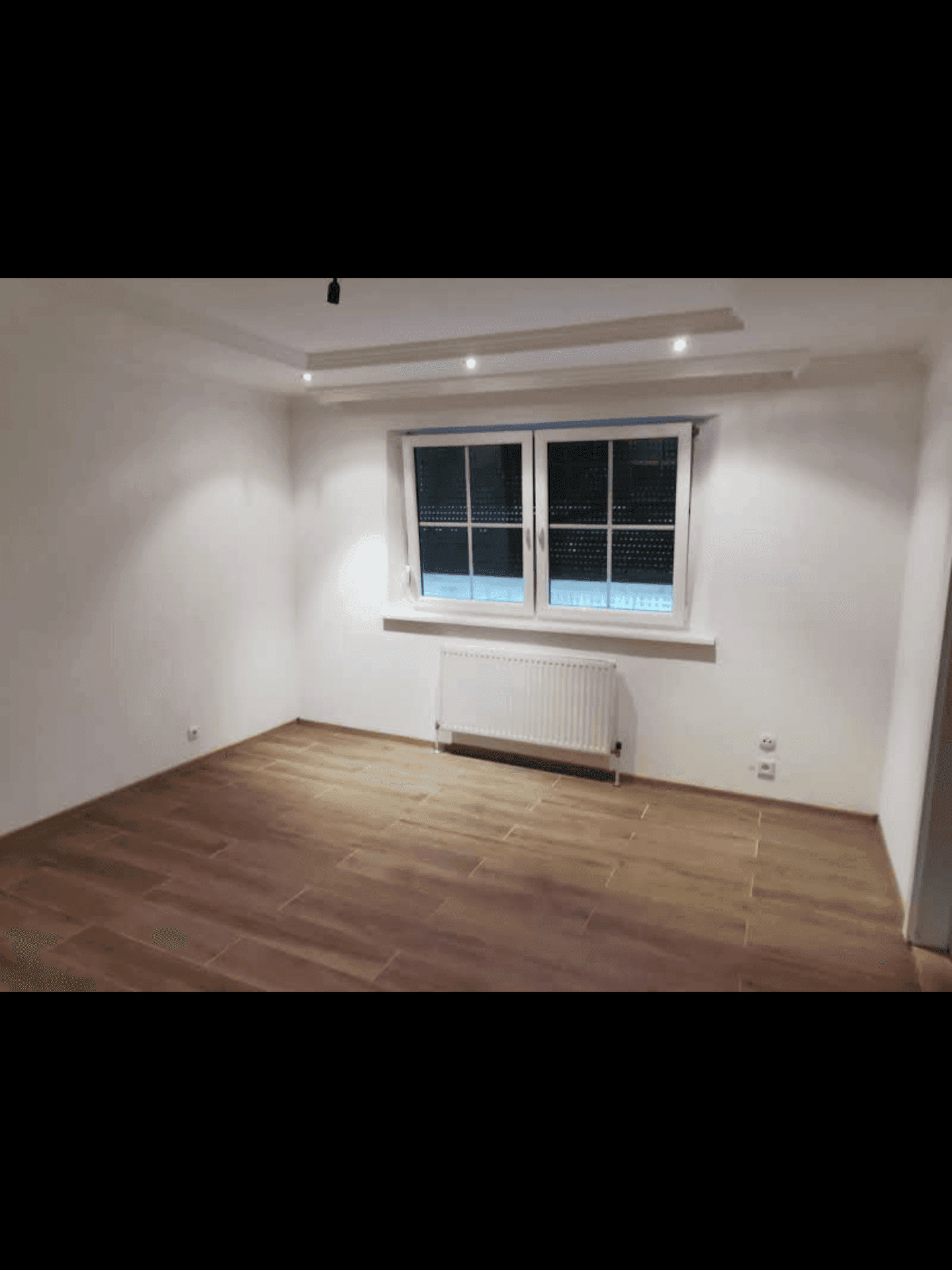 Helles Zimmer mit Holzoptik-Fliesenboden und einem Fenster mit Rollläden.