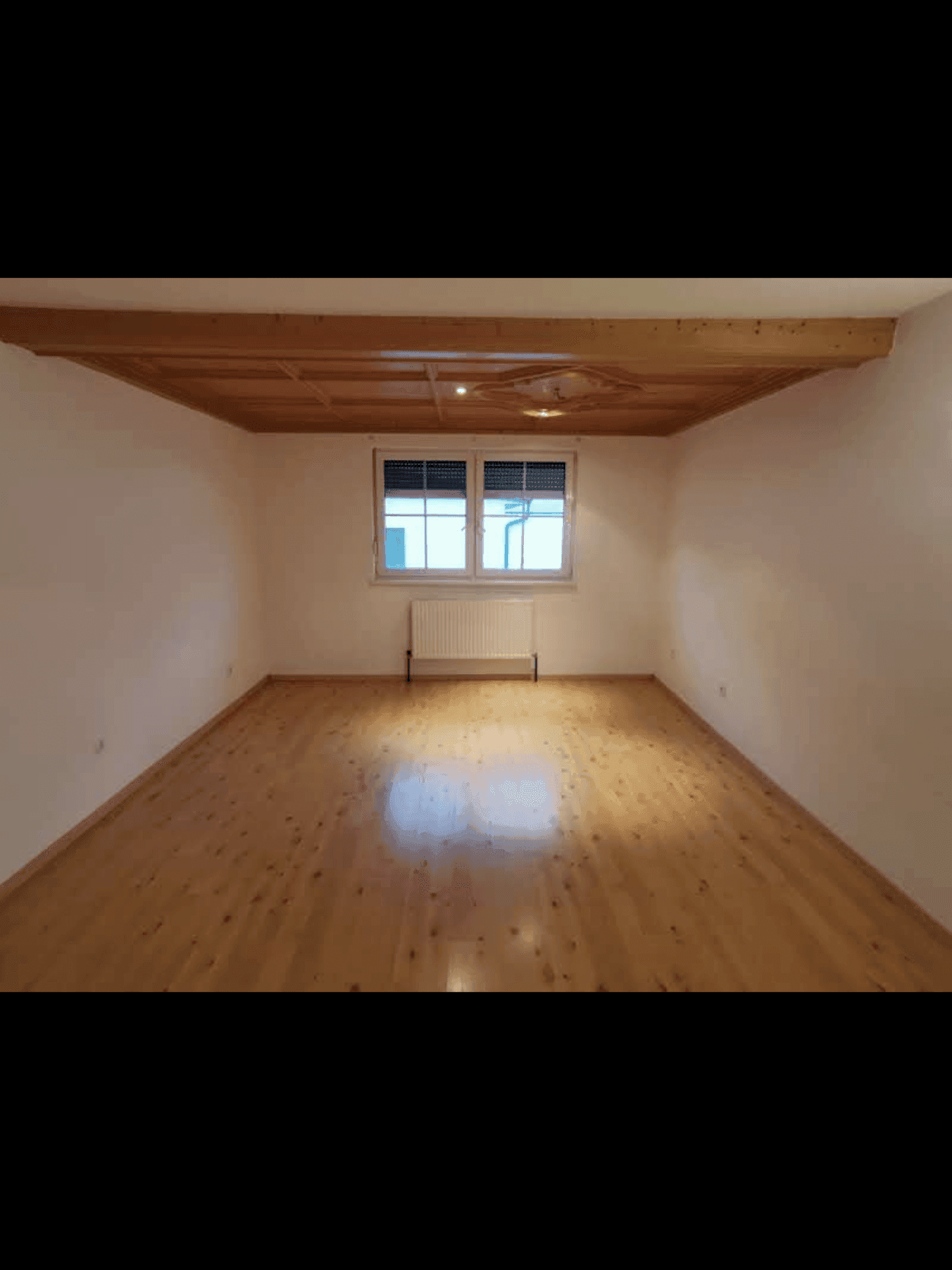 Leeres Zimmer mit hellem Holzfußboden und einer dekorativen Holzdecke.