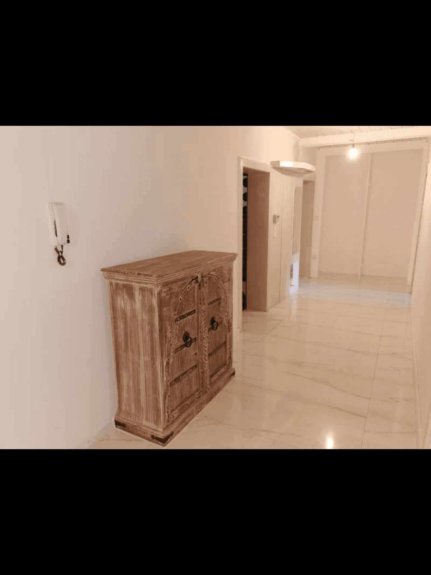 Flur mit hellem Fliesenboden und einem rustikalen Holzschrank als Dekoration.