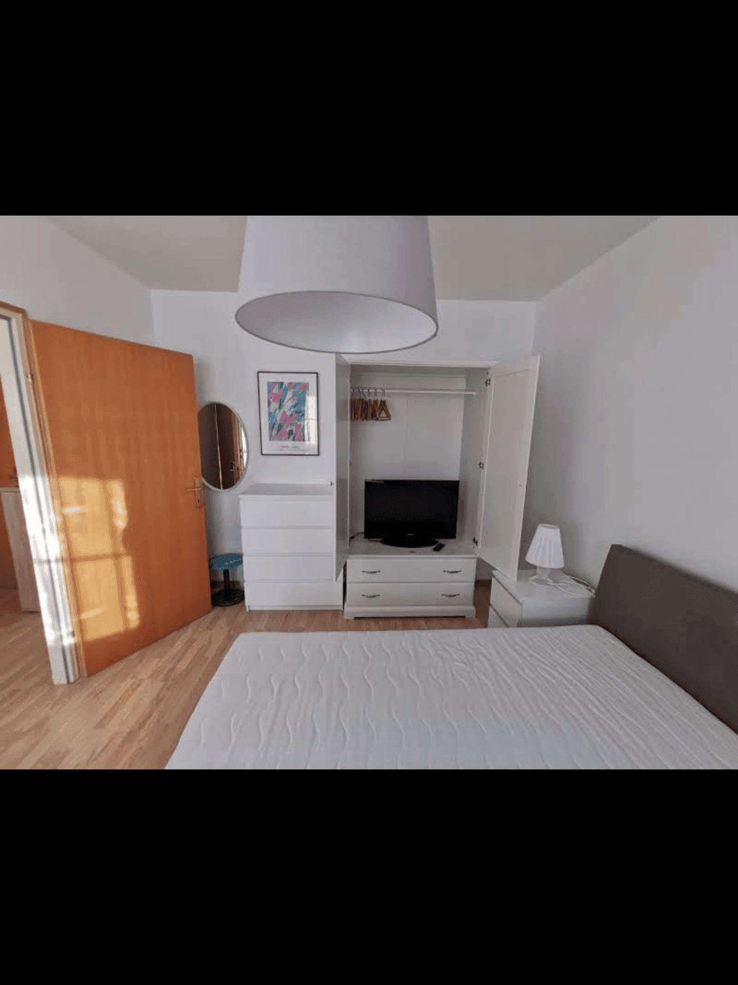 Helles Schlafzimmer mit Holzboden, einem Bett, Kommode und offenem Kleiderschrank.