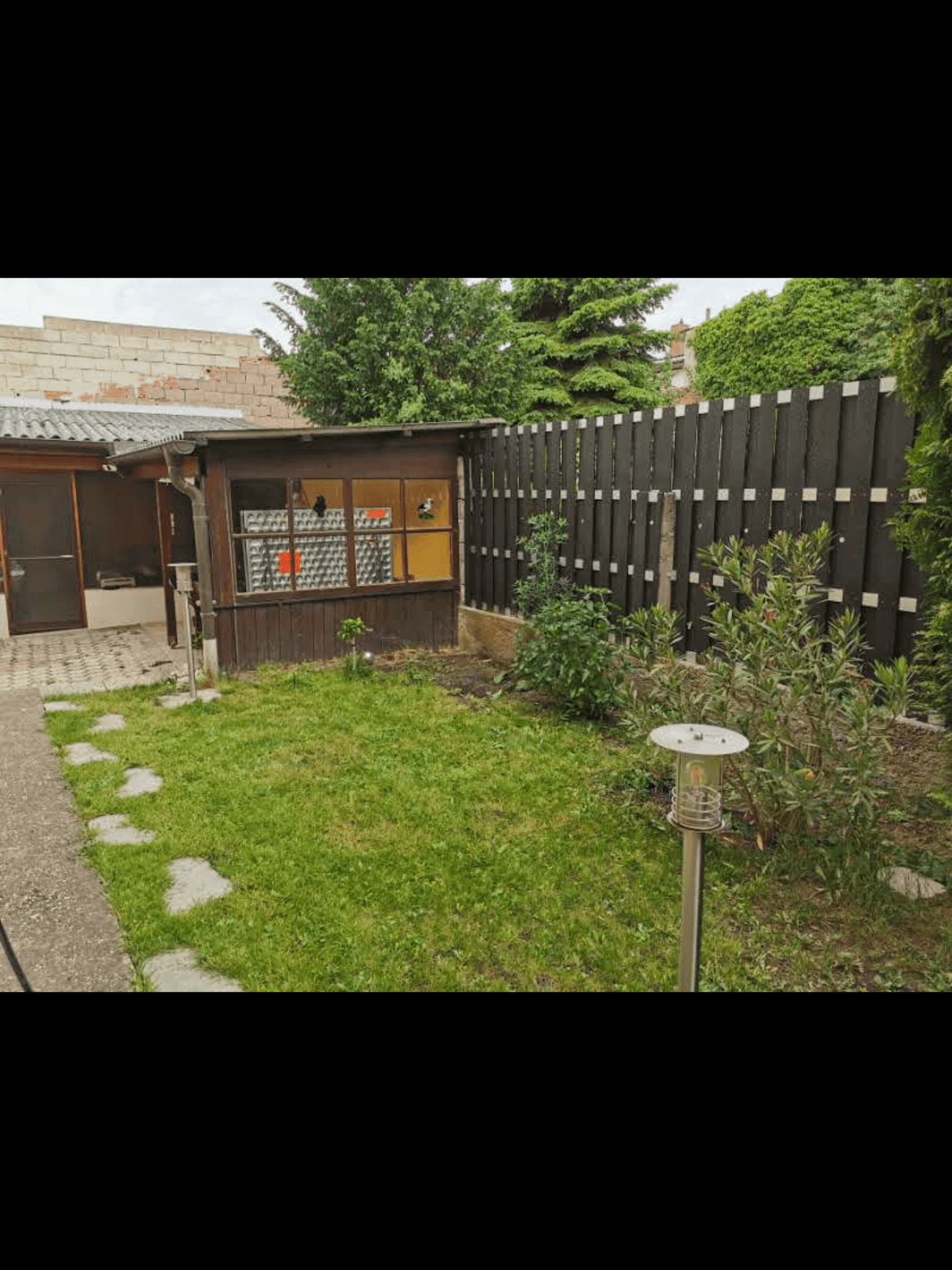 Hinterhof mit Rasenfläche, einem kleinen Gartenhaus und Holzzaun.