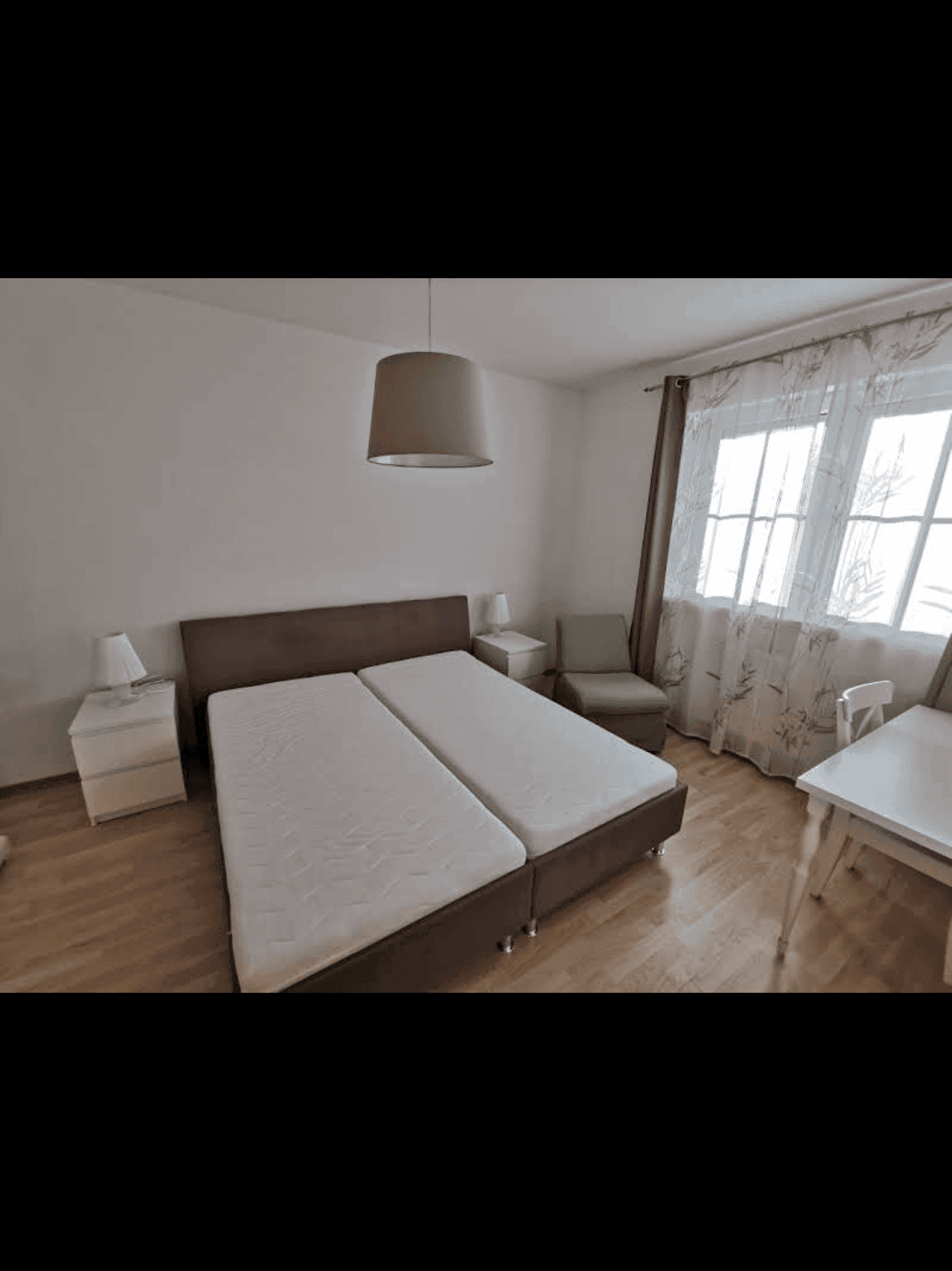 Schlafzimmer mit einem Doppelbett und einem Fenster mit hellen Vorhängen.