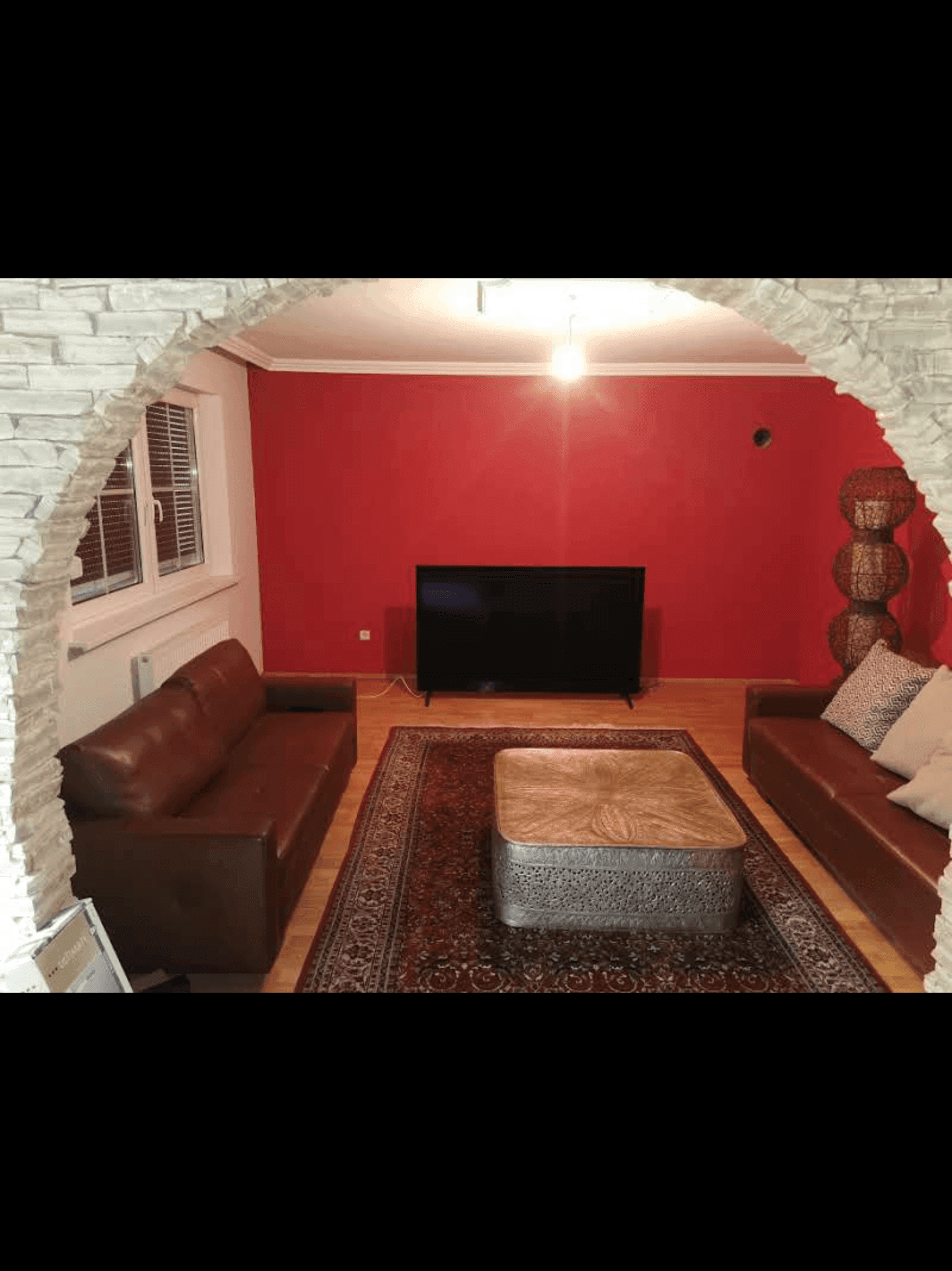 Wohnzimmer mit roten Wänden, großem Fernseher und einem dekorativen Steinbogen.
